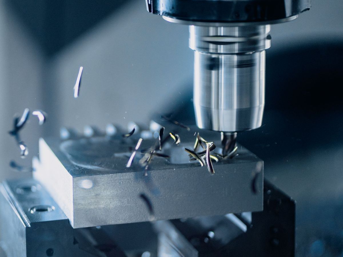 CNC freze tezgâhında metal parçayı işleyen kesici uç ve etrafa saçılan talaşlar, yakın plan