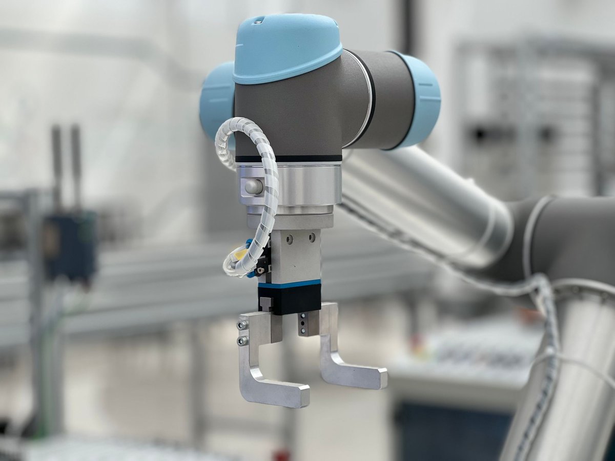 Üretim hattında gri ve açık mavi gövdeli bir robot kolunun metal tutucusu yakın planda